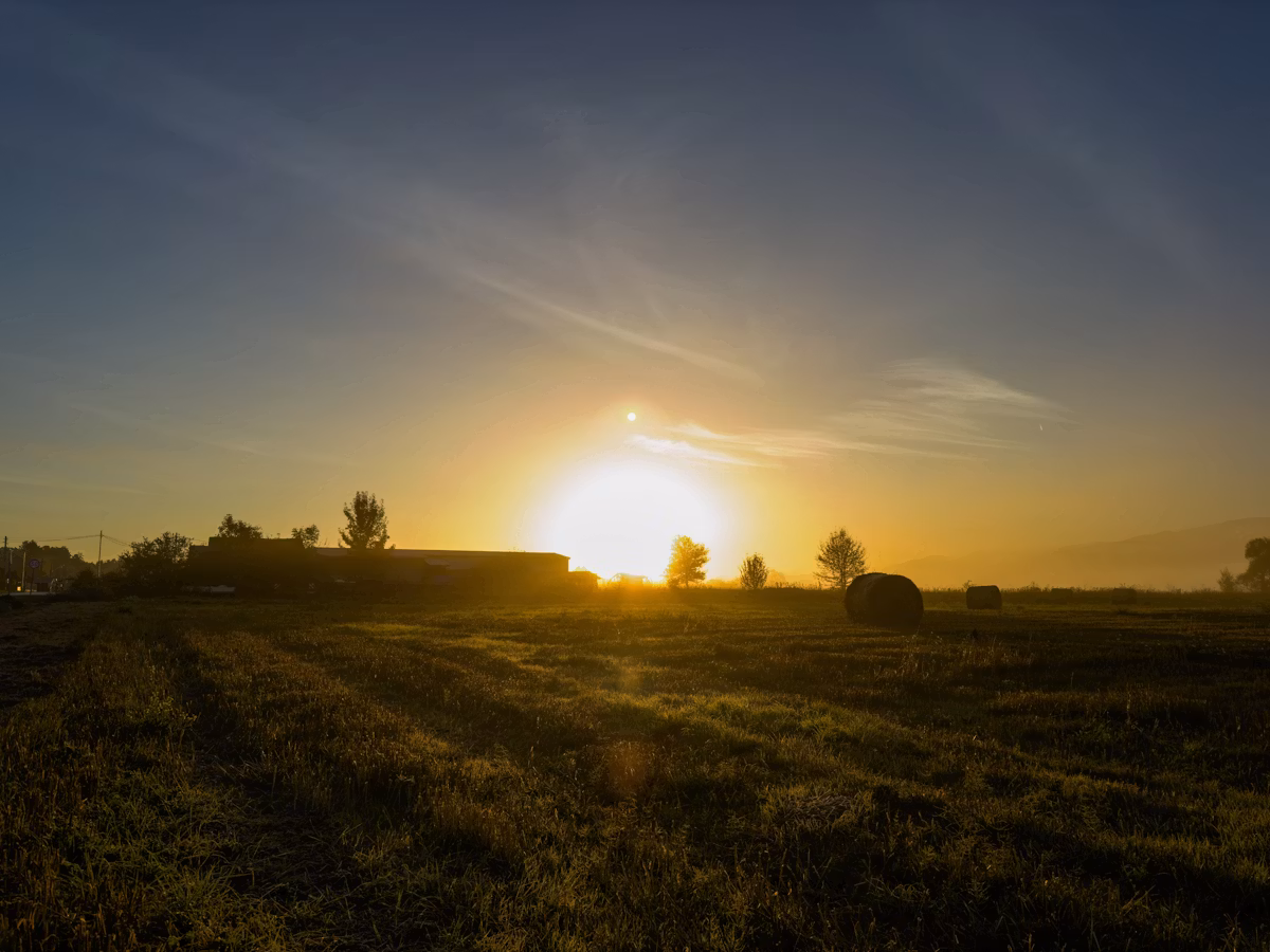 Golden hour light over a countryside farm field with hay bales in early autumn